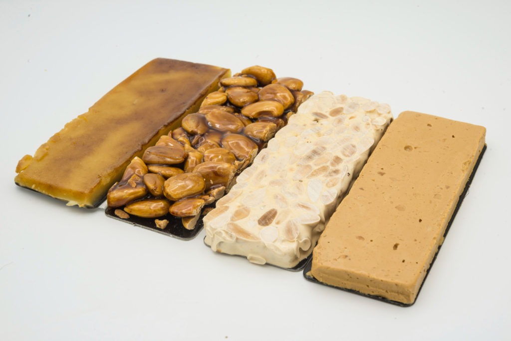 "Découvrez votre Turron idéal chez María Simona: explorez notre guide complet pour choisir le Turron parfait et les meilleurs accords avec des vins, pour des moments gourmands inoubliables." Variété de turróns Maria Simona alignés sur un fond blanc
